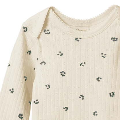 Close-up of a cream-colored sweater with small green floral patterns on a white background.