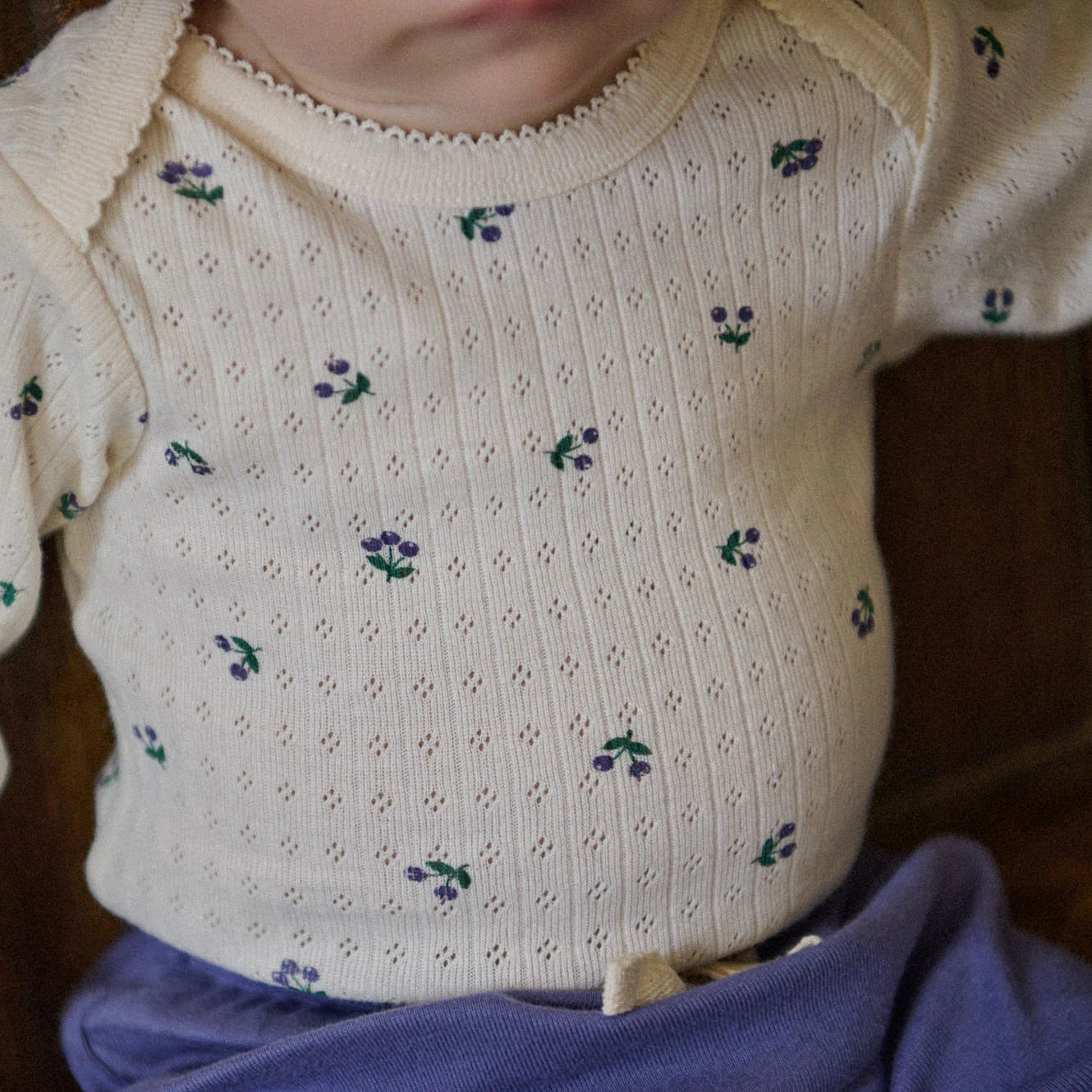 Close-up of a baby wearing a white knitted sweater with floral patterns.