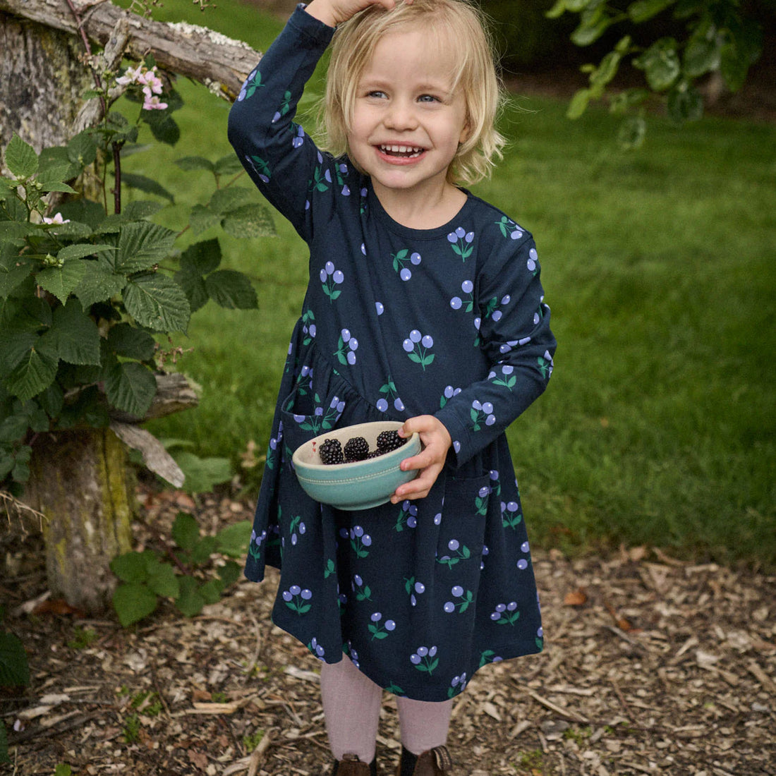 Young girl in a garden holding a bowl of blackberries