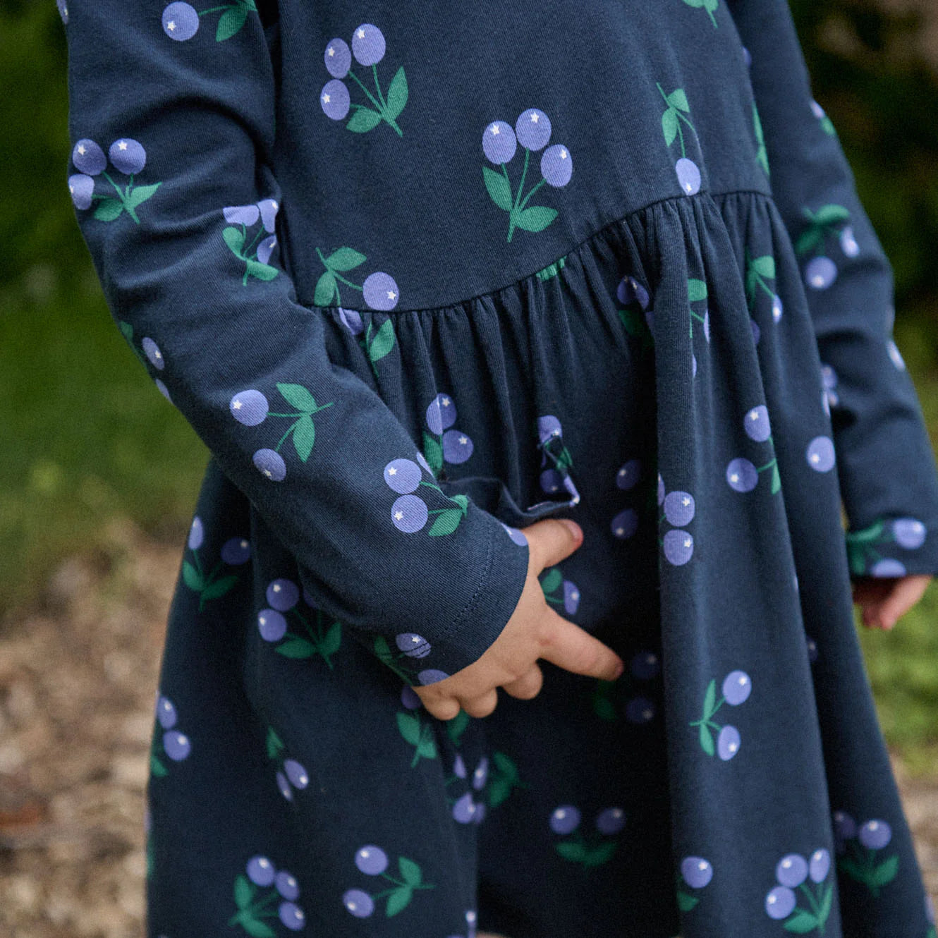 Navy dress with cherry pattern worn by a child, blurred natural background