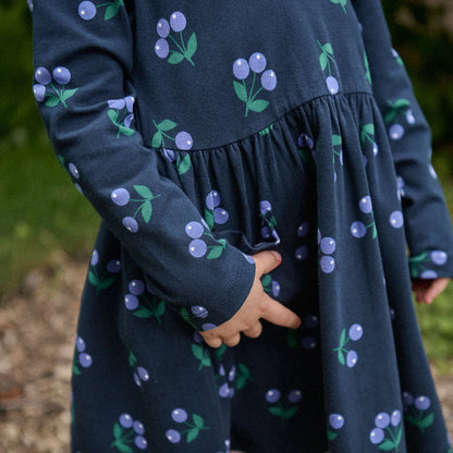 Navy dress with cherry pattern worn by a child, blurred natural background