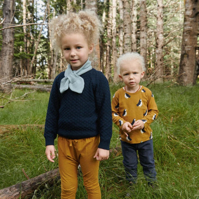 Two children standing in a forest, wearing matching outfits.
