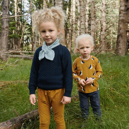 Two children standing in a forest, wearing matching outfits.