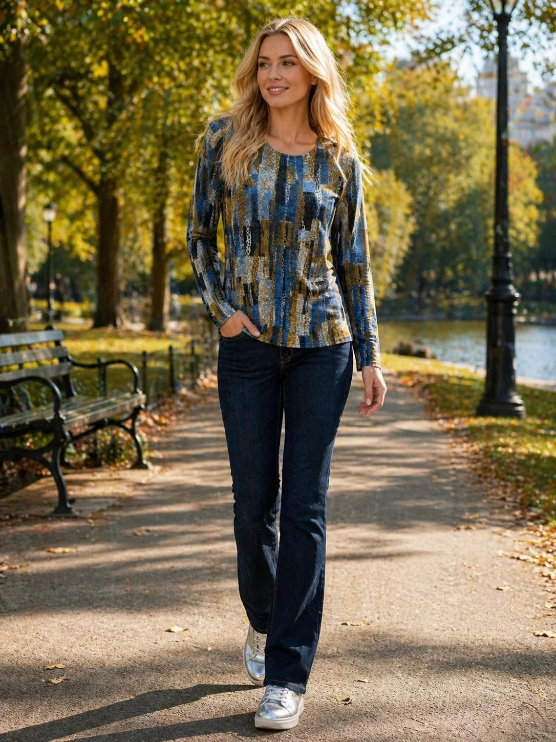 Woman walking in a park wearing a patterned shirt and jeans.