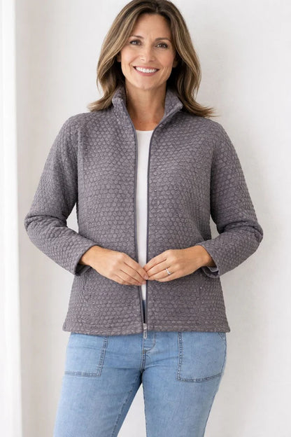 Woman wearing a gray quilted jacket and blue jeans against a white background