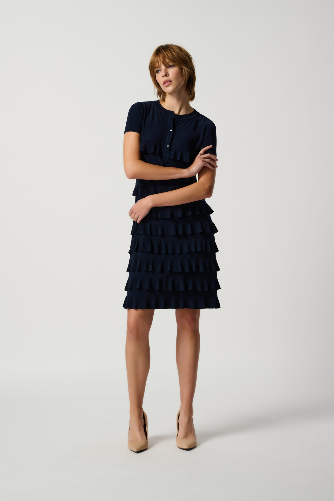 A navy joseph ribkoff ruffle dress with short sleeves, featuring a ruffled design around the entire dress. A model is posing with a hand by her side.