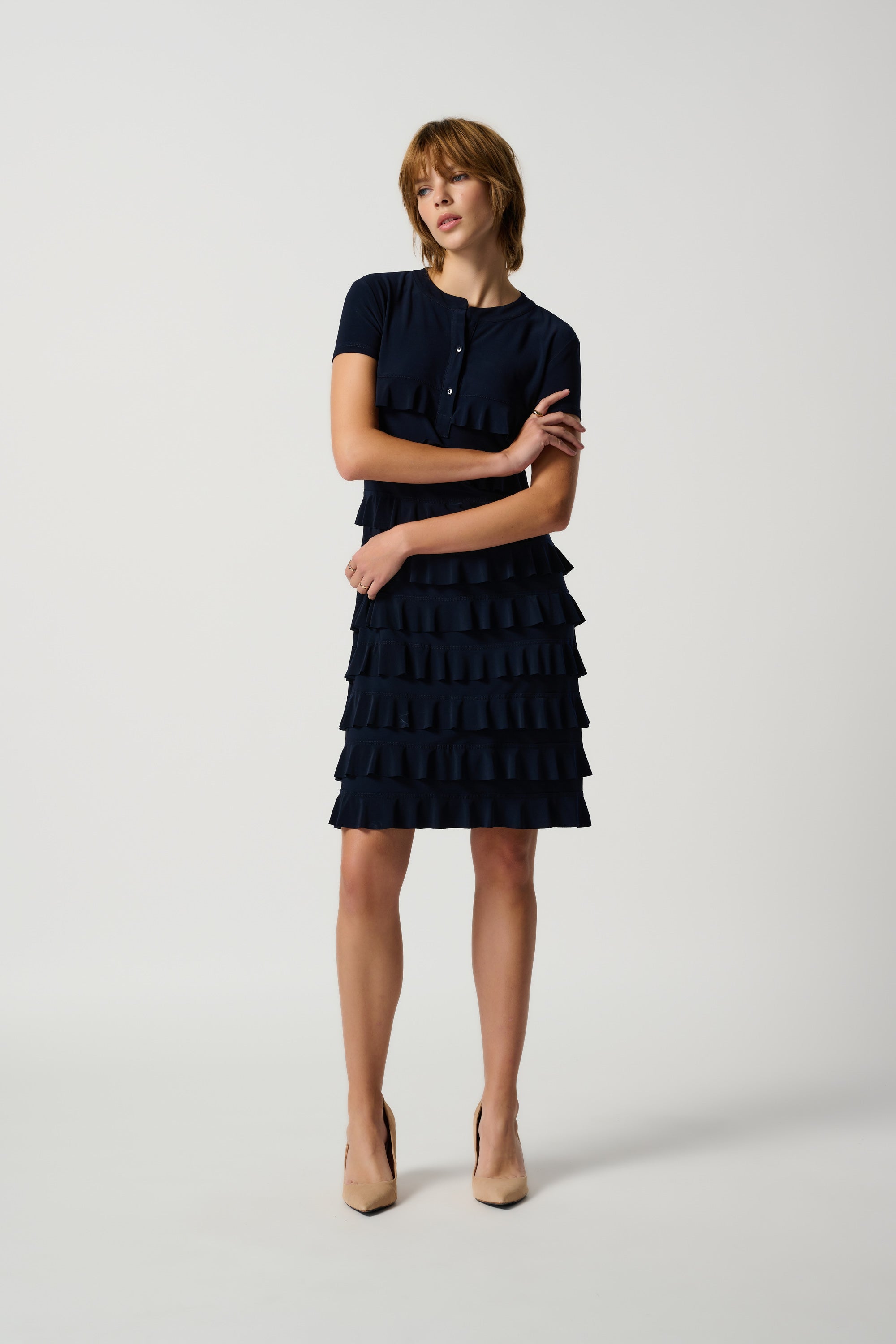 A navy joseph ribkoff ruffle dress with short sleeves, featuring a ruffled design around the entire dress. A model is posing with a hand by her side.