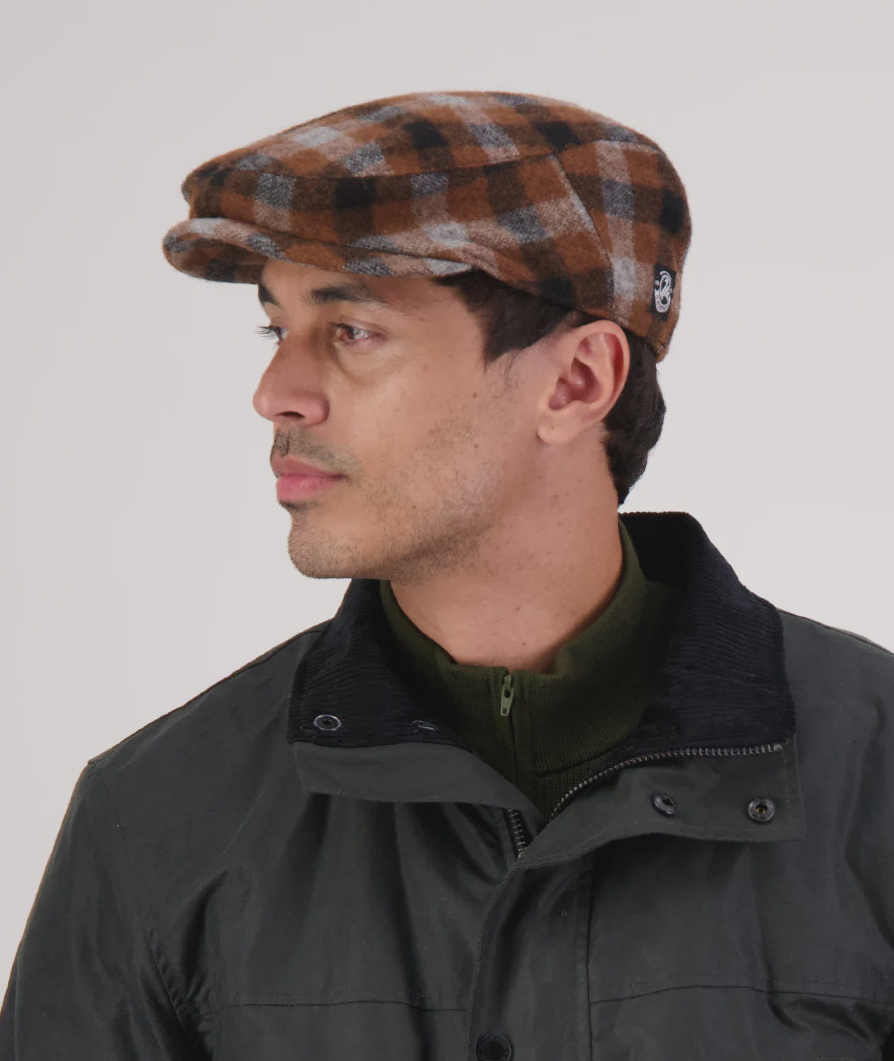 Man wearing a checkered cap and dark jacket on a plain background