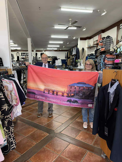 Two people holding a towel with a scenic design in a store setting.