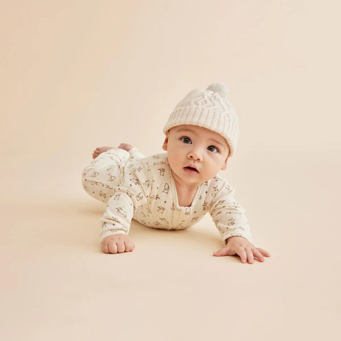 Baby in a white outfit and hat crawling on a beige surface