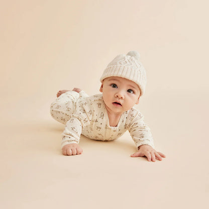 Baby in a white outfit and hat crawling on a beige surface