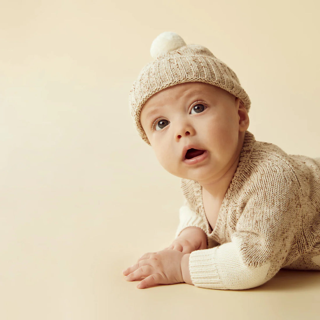 Baby wearing a knitted hat and sweater on a beige background