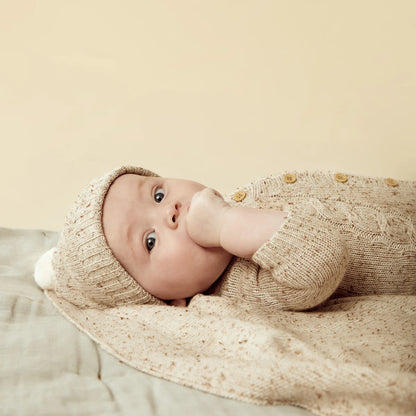 Baby in a knitted outfit and hat lying on a soft surface with a neutral background