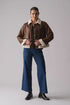 Person wearing a brown shearling jacket with white fur trim, blue jeans, and black shoes on a gray background
