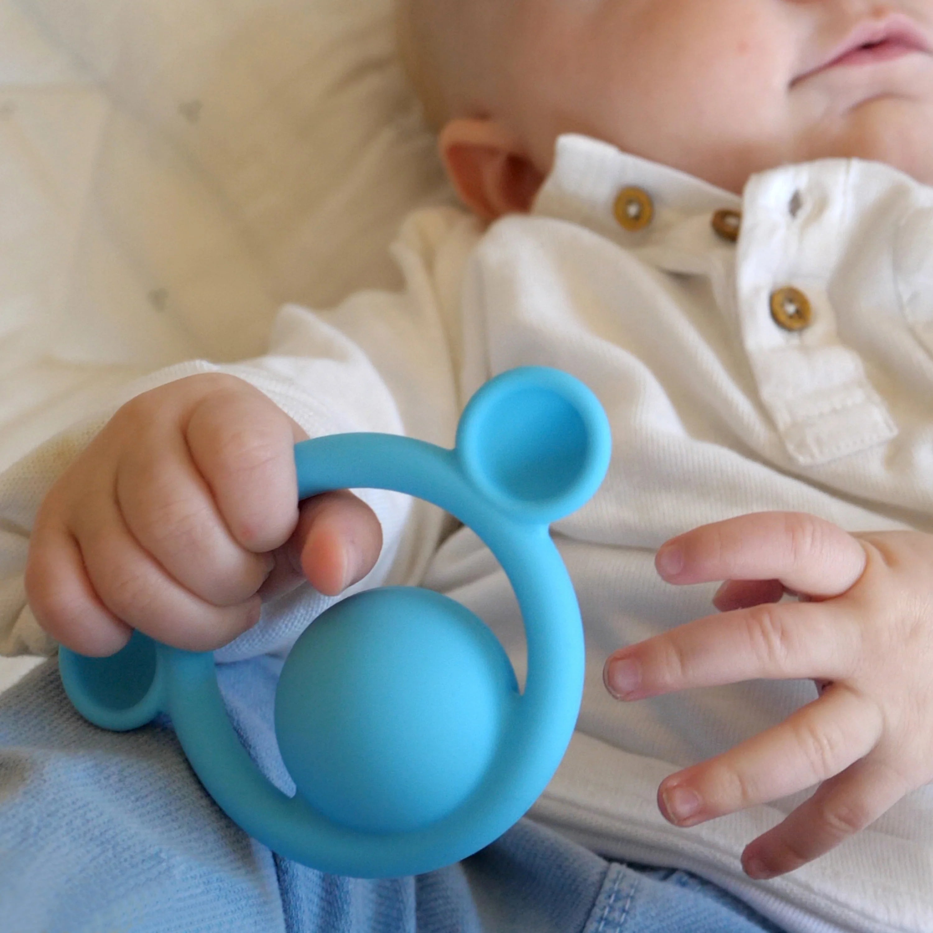 Baby holding a blue teething ring with a soft focus background
