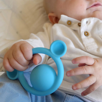 Baby holding a blue teething ring with a soft focus background