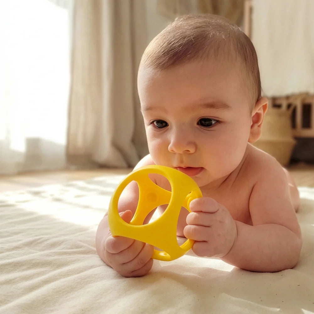 Baby holding a yellow toy on a bed
